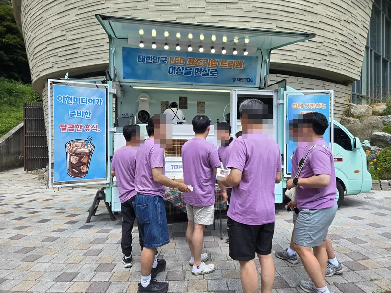 단체티를 입은 임직원들이 민트색 트럭에서 음료를 받는 모습